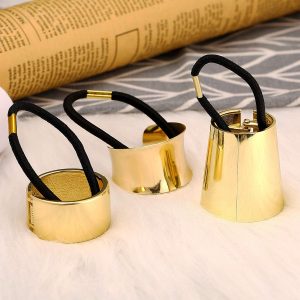 Gold hair cuffs with black elastic bands on a white surface, with newspaper in the background